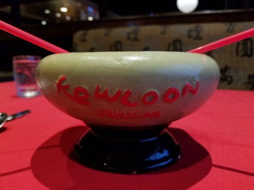 A green bowl with "Kowloon" written on it, placed on a red tablecloth in a restaurant setting.