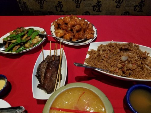 A table set with various Chinese dishes: fried rice, sweet and sour chicken, skewered meat, and a dessert.