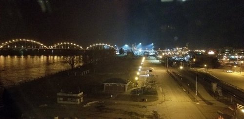 Night view of a river with illuminated bridges and a city skyline, featuring streetlights and a darkened landscape.