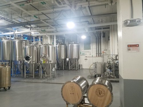 Industrial brewing facility with stainless steel tanks, pipes, and equipment in a clean, well-lit environment.