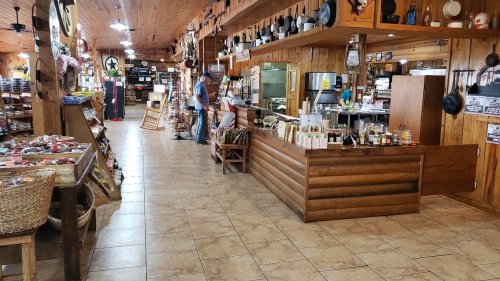 A rustic store interior with wooden decor, shelves of goods, and a checkout counter. A customer browses in the background.