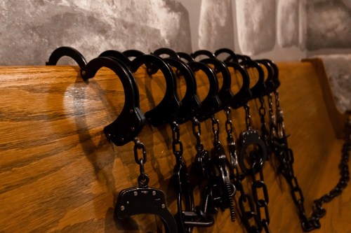 A row of black handcuffs hanging on a wooden rack against a textured wall.