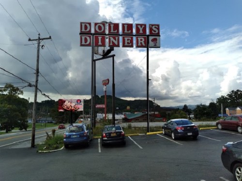 Sign for Dolly's Diner with cars parked in the lot and a cloudy sky in the background.