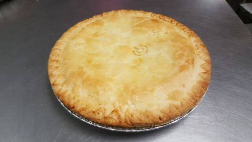 A golden-brown pie with a flaky crust, resting on a silver pie tin against a metallic surface.