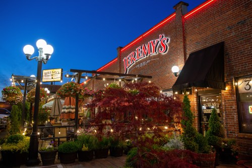 Exterior of Jeremy's restaurant at dusk, featuring warm lights, hanging plants, and a cozy outdoor seating area.