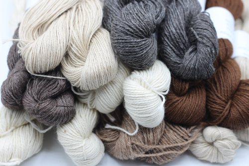 A variety of yarn skeins in neutral tones, including cream, brown, and gray, stacked together.