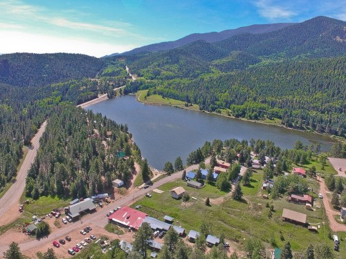 Aerial view of a small lakeside town surrounded by lush green forests and mountains under a clear blue sky.