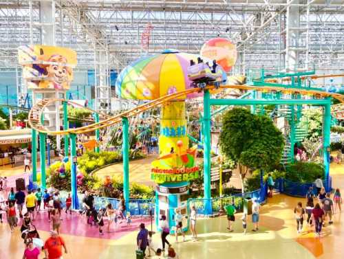 A vibrant indoor amusement park with a roller coaster, colorful attractions, and crowds of people enjoying the space.