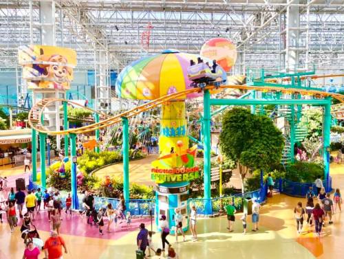 A vibrant indoor amusement park with a roller coaster, colorful attractions, and crowds of people enjoying the space.