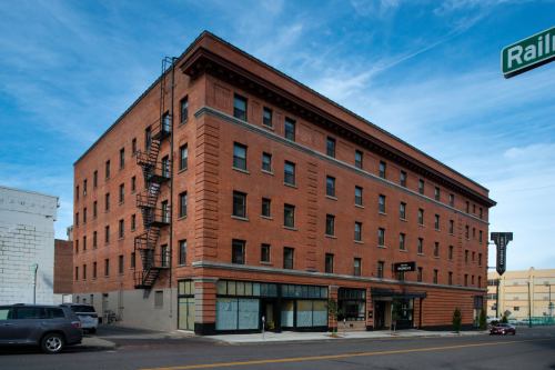 A four-story brick building with large windows and a fire escape, located at the corner of a street.