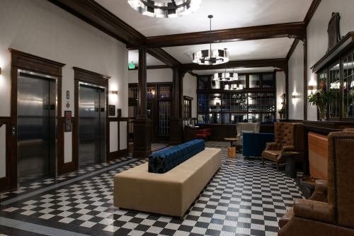 A stylish lobby with checkered flooring, modern lighting, and a mix of seating areas, including a long beige bench.