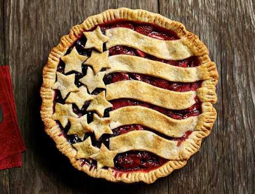 A cherry pie decorated with a flag design, featuring stars and stripes on a wooden surface.