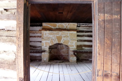 View of a rustic interior with a stone fireplace and wooden beams, framed by a dark wooden doorway.