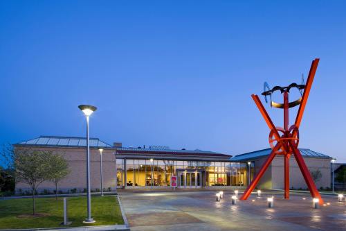 Modern building with large red sculpture in front, illuminated by streetlights at dusk. Green grass and trees nearby.