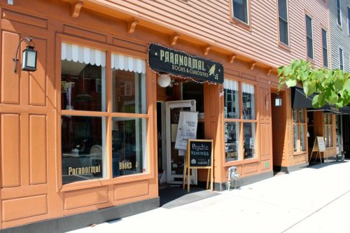 A storefront labeled "Paranormal Books & Curiosities" with a sign for psychic readings, featuring a charming facade.