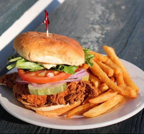 A crispy fried chicken sandwich with lettuce, tomato, pickles, and fries on a plate.