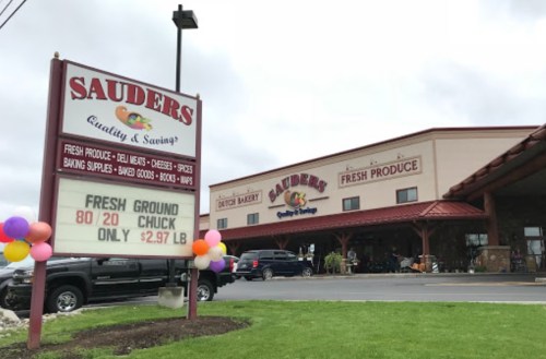 A storefront with a sign advertising fresh produce and ground chuck, decorated with colorful balloons.
