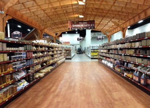 A spacious grocery store aisle lined with shelves of spices and condiments under a wooden ceiling.