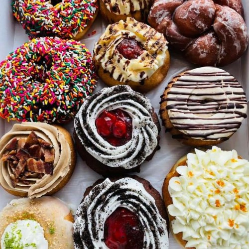 A variety of colorful donuts and pastries arranged in a box, featuring sprinkles, frosting, and fruit toppings.