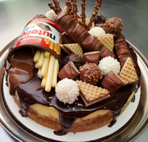 A decadent chocolate cake topped with Nutella, wafers, chocolate truffles, and decorative chocolate sticks.