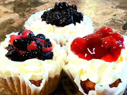 Three cupcakes with white frosting topped with blackberries, mixed berries, and cherry sauce.