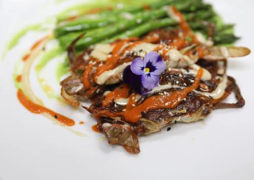 A gourmet dish featuring crab topped with sauces, garnished with a flower, and served with asparagus on a white plate.