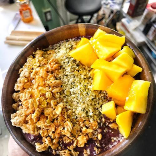 A bowl of smoothie topped with granola, hemp seeds, and fresh mango chunks.