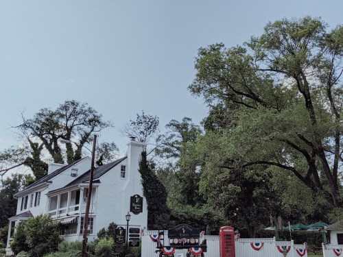 A charming white building with a porch, surrounded by trees and decorative bunting, under a clear blue sky.