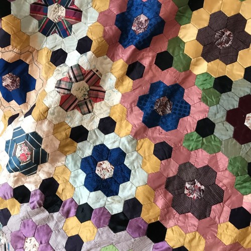 A colorful quilt featuring a hexagonal patchwork design with various floral and geometric patterns.