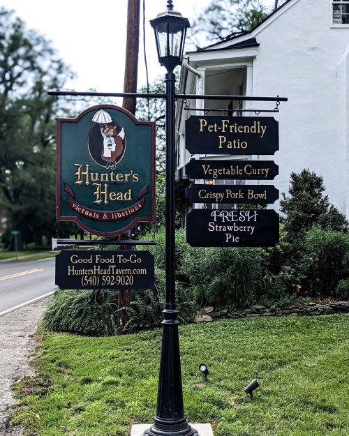 Signpost for Hunter's Head Tavern featuring directions to a pet-friendly patio, menu items, and contact information.