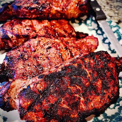 Grilled steaks with a charred exterior, arranged on a plate with a knife in the background.