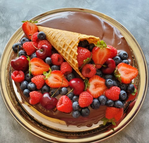 A chocolate cake topped with a waffle cone and an assortment of fresh berries, including strawberries, blueberries, and raspberries.