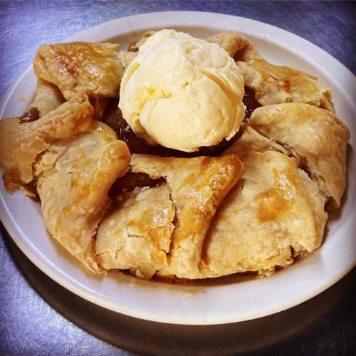 A slice of pie with a flaky crust, filled with fruit, topped with a scoop of vanilla ice cream on a white plate.