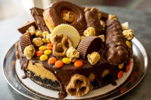 A decadent cake topped with donuts, chocolate bars, popcorn, and colorful candies on a silver platter.