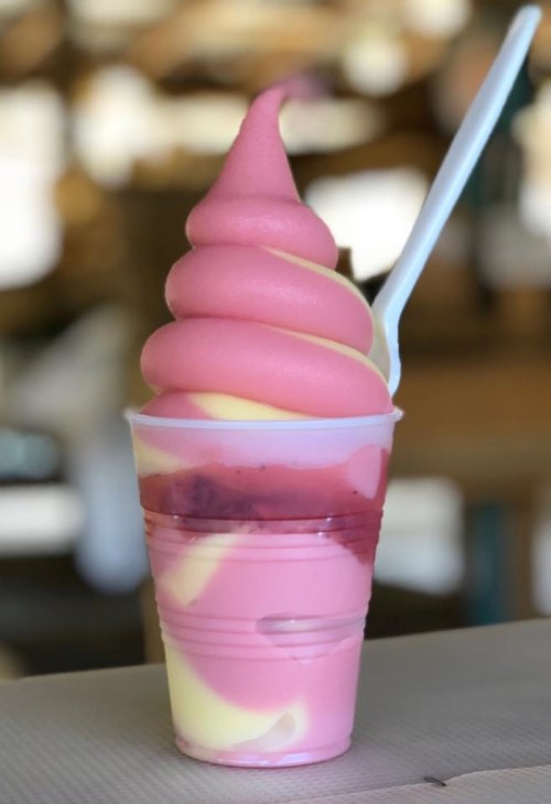 A cup of soft-serve ice cream with pink and yellow swirls, topped with a spoon.