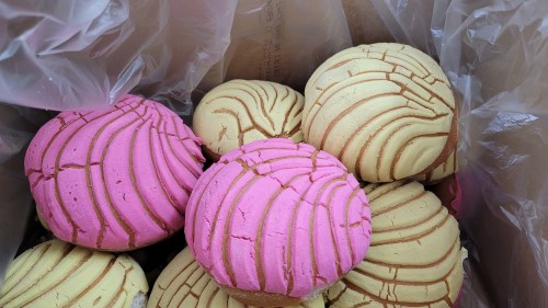A box filled with colorful conchas, featuring pink and yellow varieties with a textured, striped pattern.