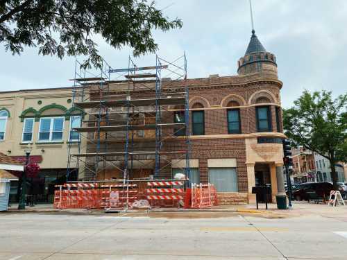 Historic building under renovation, surrounded by scaffolding and construction barriers, with a cloudy sky above.