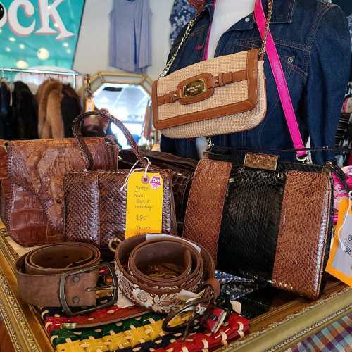 A display of various handbags and belts in a vintage shop, showcasing different textures and styles.