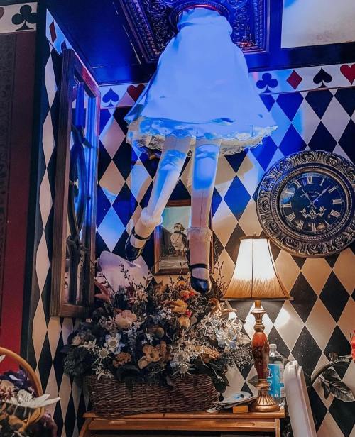 A whimsical display featuring a floating dress and legs above a floral arrangement in a patterned room.