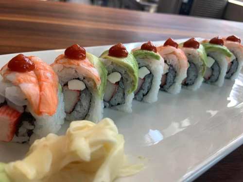 A plate of colorful sushi rolls topped with sauce, accompanied by pickled ginger on the side.
