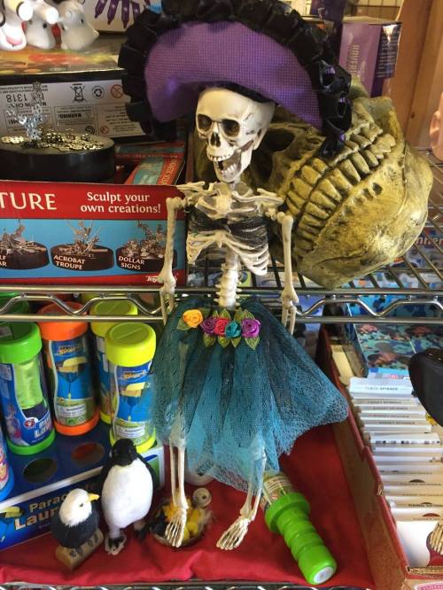 A decorative skeleton wearing a purple hat and a blue skirt, surrounded by colorful toys and crafts.