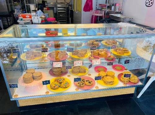 A display case filled with various cookies on colorful plates, labeled with names and prices.