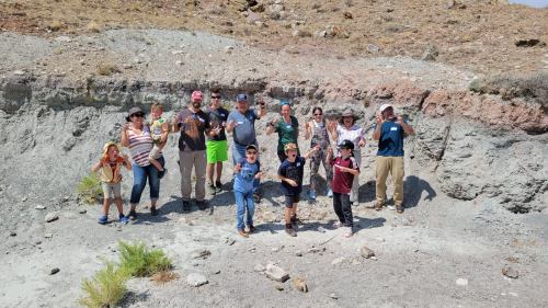 A group of people, including children, poses happily in front of a rocky landscape on a sunny day.