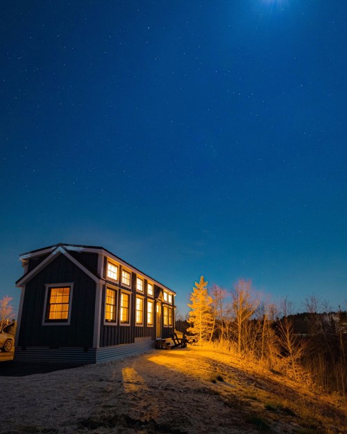 A cozy house illuminated at night, surrounded by trees under a starry sky and a bright moon.