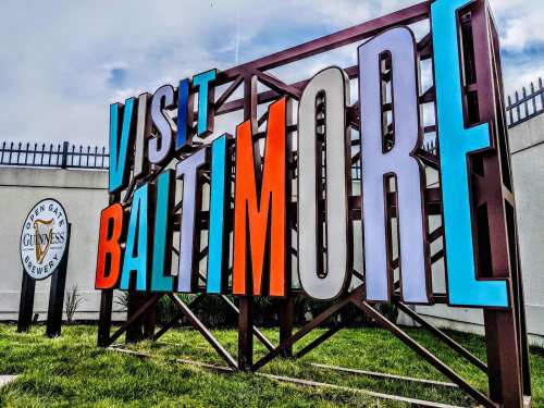 Colorful "Visit Baltimore" sign in front of the Guinness Open Gate Brewery, surrounded by green grass.