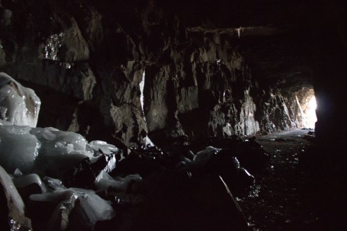 A dark cave interior with icy formations and a bright light at the far end, highlighting the rocky walls.