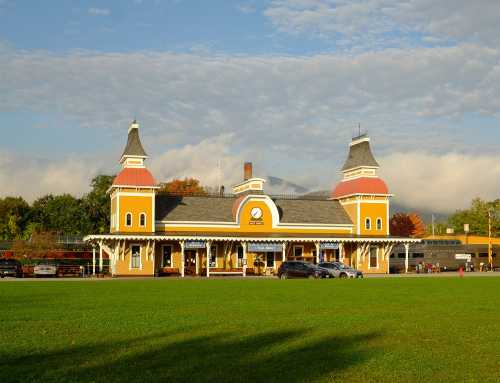 A charming yellow train station with two towers, set against a blue sky and green lawn.