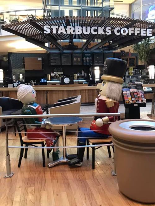 Two whimsical nutcracker figures sit at a table in a Starbucks, surrounded by a modern café setting.