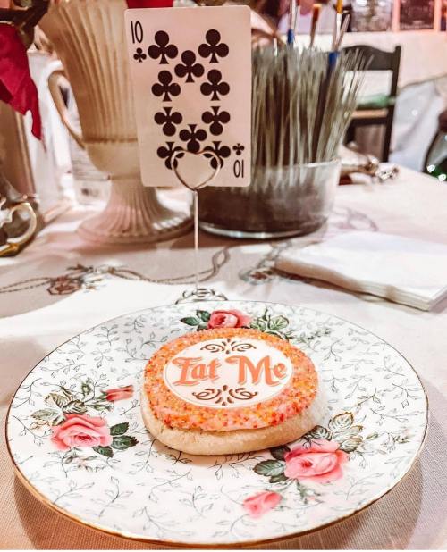 A decorative plate holds a cookie with "Eat Me" written on it, alongside a playing card displaying the number 10 of clubs.