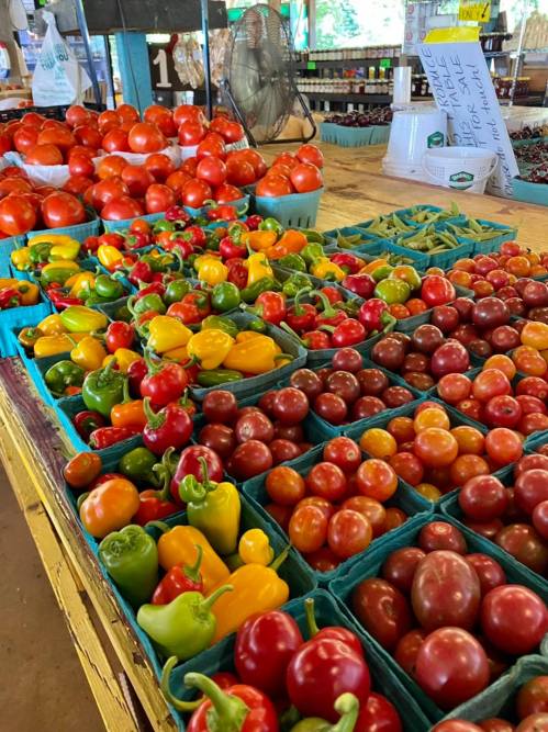 A vibrant display of various tomatoes and bell peppers in baskets at a market stall.